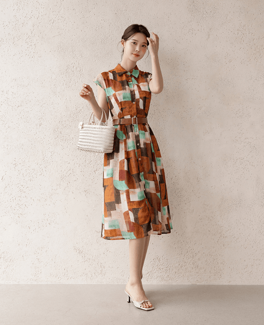 Woman wearing a chic shirt dress with cap sleeves, classic collar, and faux leather belt, holding a woven handbag.