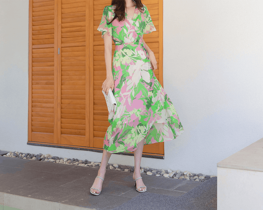 Woman wearing chiffon wrap dress with floral pattern, tulip hem, and feminine silhouette, set against wooden shutters.