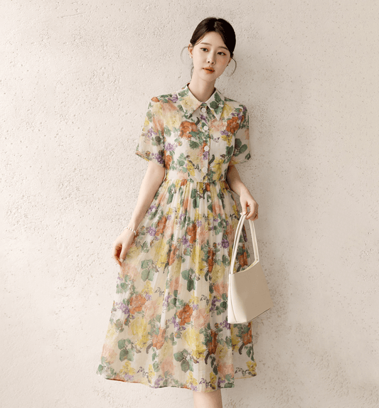 Woman wearing a romantic floral dress with pintuck details and a collar neckline, holding a white handbag, against a white background.
