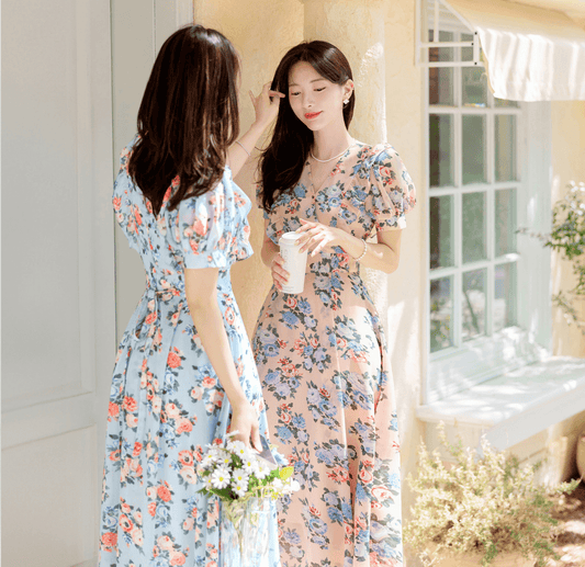 Two women wearing romantic floral chiffon dresses with V-necklines, short puff sleeves, in pink and blue, enjoying a sunny day.