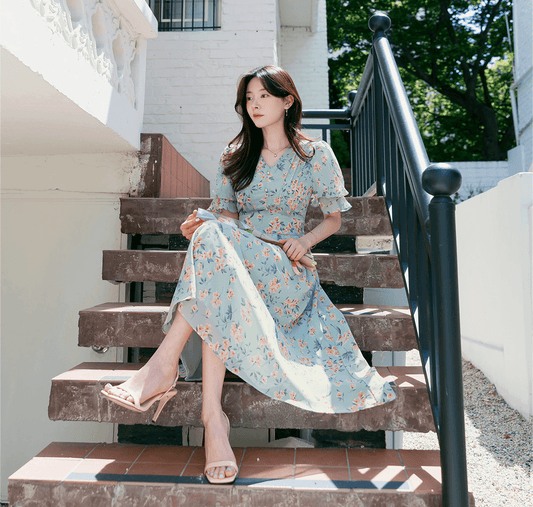 Woman wearing a V-Neck Puff Sleeve Floral Chiffon Dress in Breezy Blue sitting on steps, showcasing spring floral fashion.