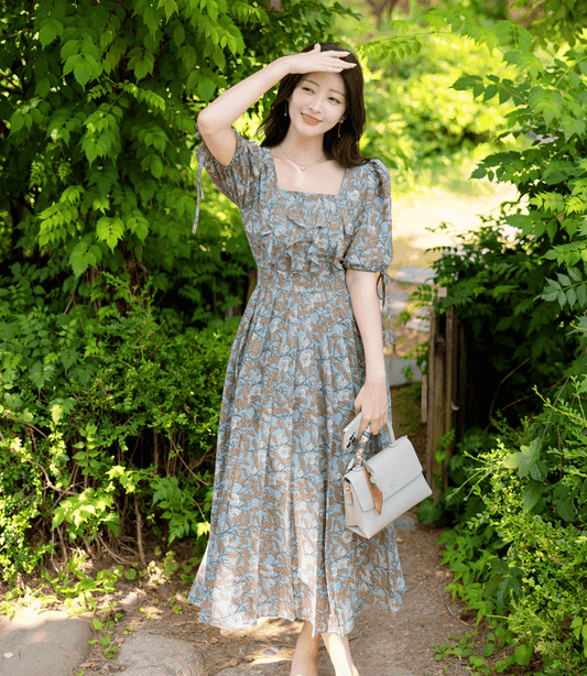 Woman wearing a pleated dress with slit sleeves and ribbon ties, standing in a garden
