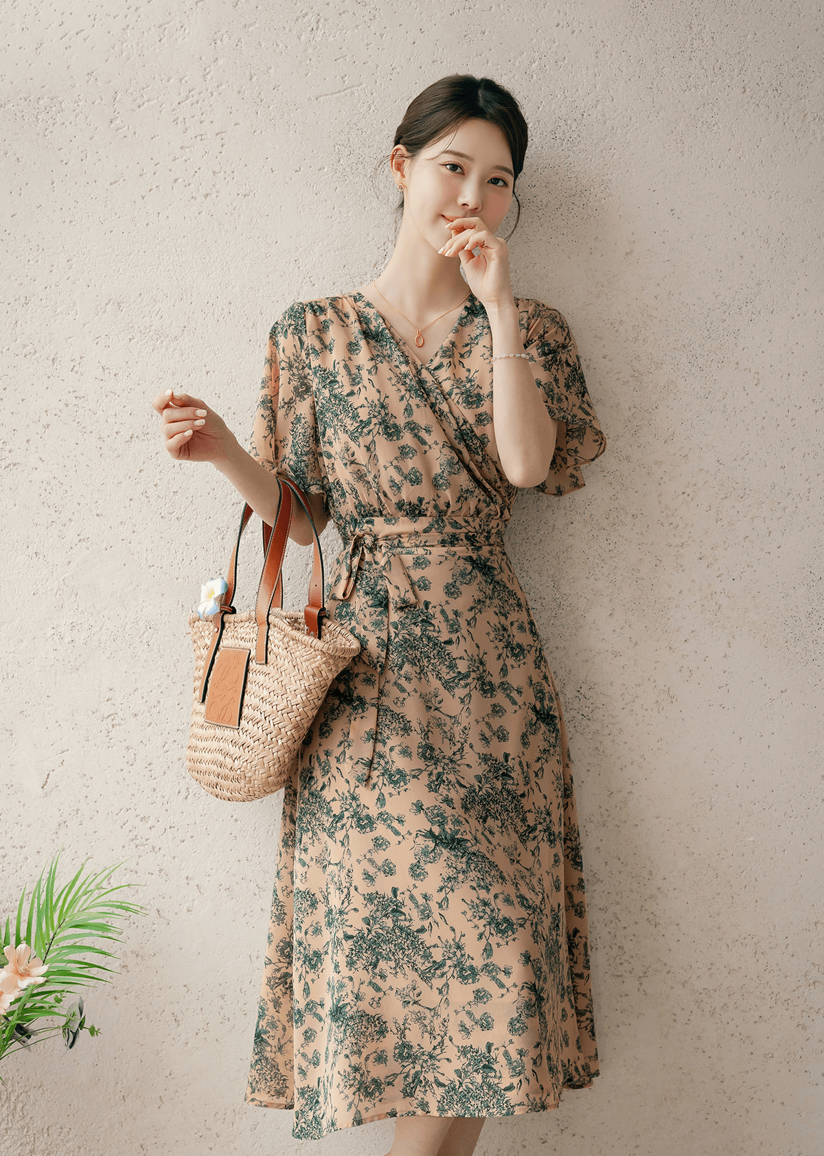 Woman wearing a goddess-inspired wrap dress with graceful wing sleeves, holding a woven bag, showcasing a summer fashion look.