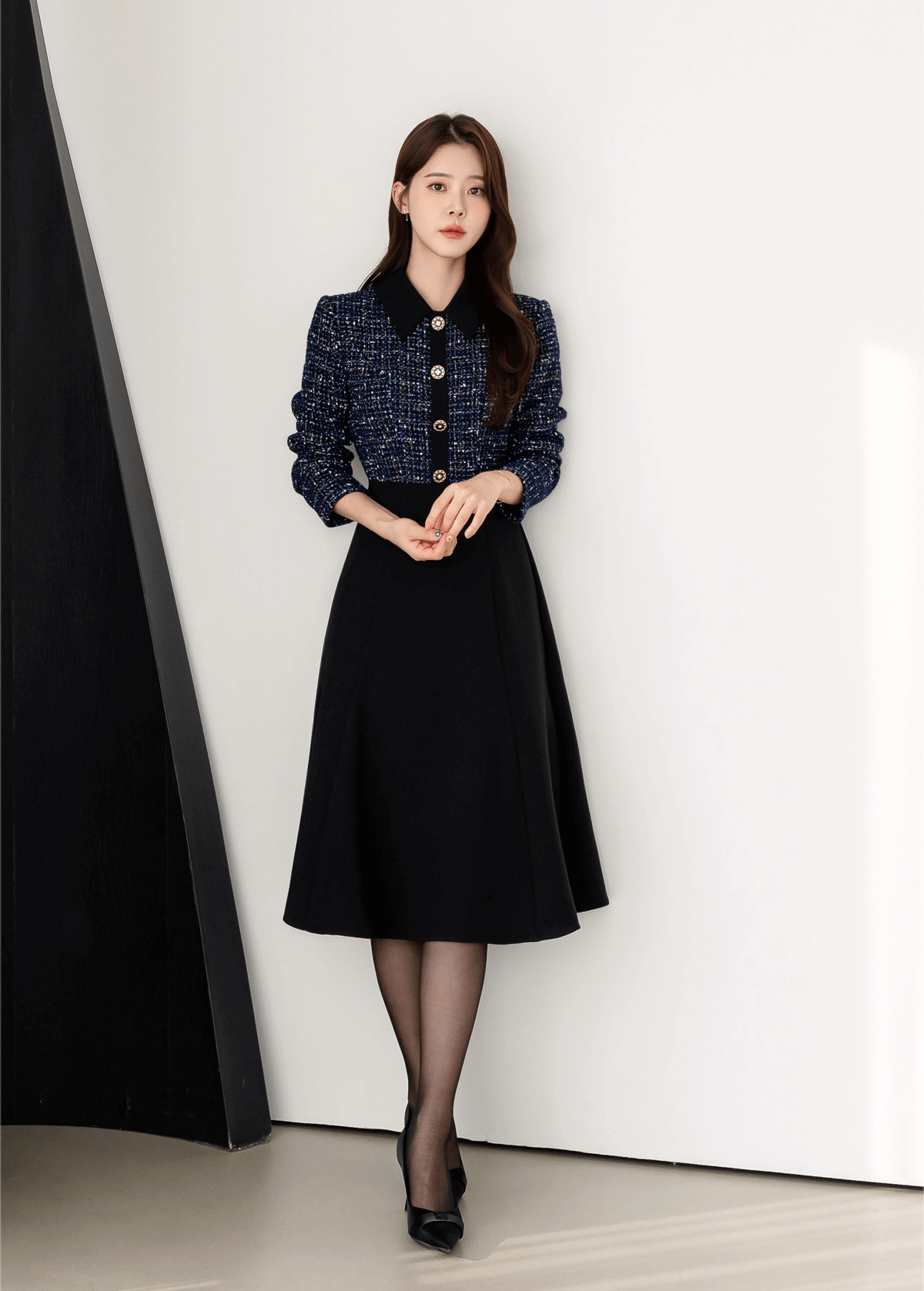 Two-tone navy tweed and black flare dress with gold button detail, worn by woman, showcasing elegant design and contrast.