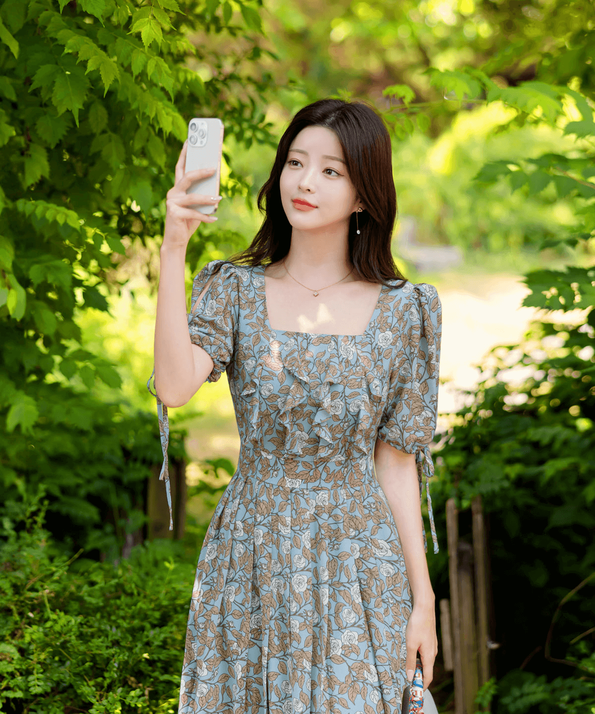 Woman wearing a pleated dress with slit sleeves and ribbon ties, taking a selfie in a garden setting.