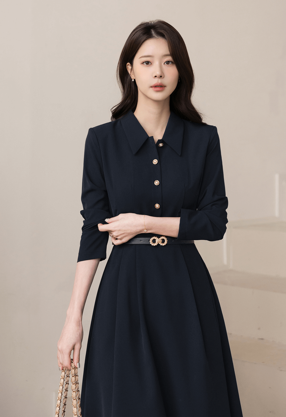 Elegant navy flare dress with long sleeves, belted waistline, and structured collar, worn by a woman holding a handbag.