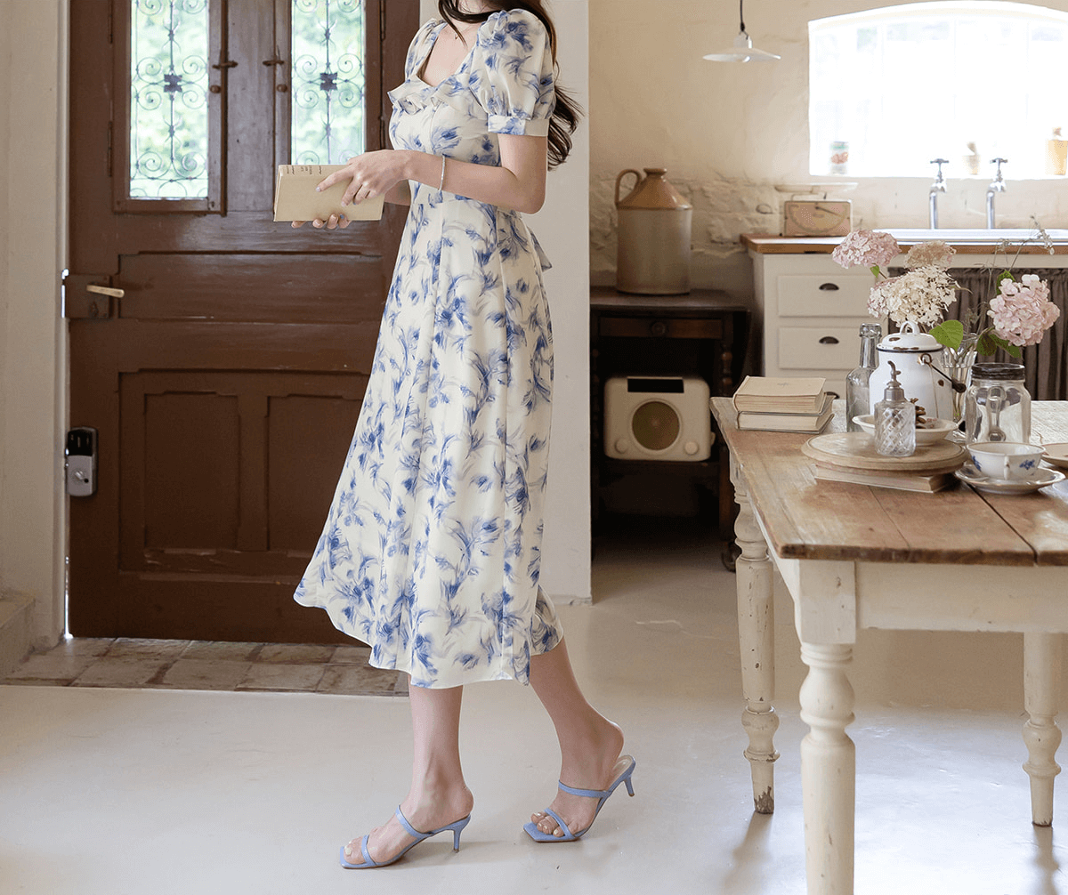 Elegant chiffon dress with blue-violet abstract print and square ruffle neckline, worn by a model in a bright vintage kitchen