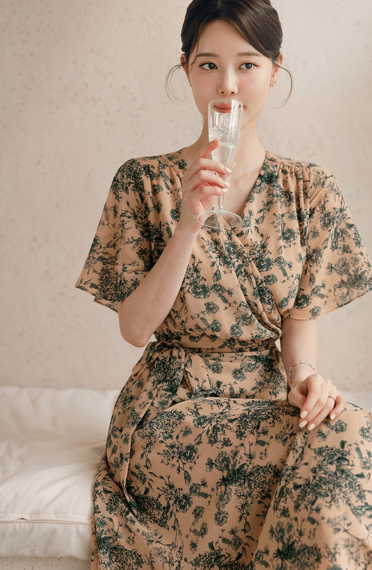 Woman wearing a goddess-inspired wrap dress with graceful wing sleeves, sipping a drink. Elegant and feminine fashion.