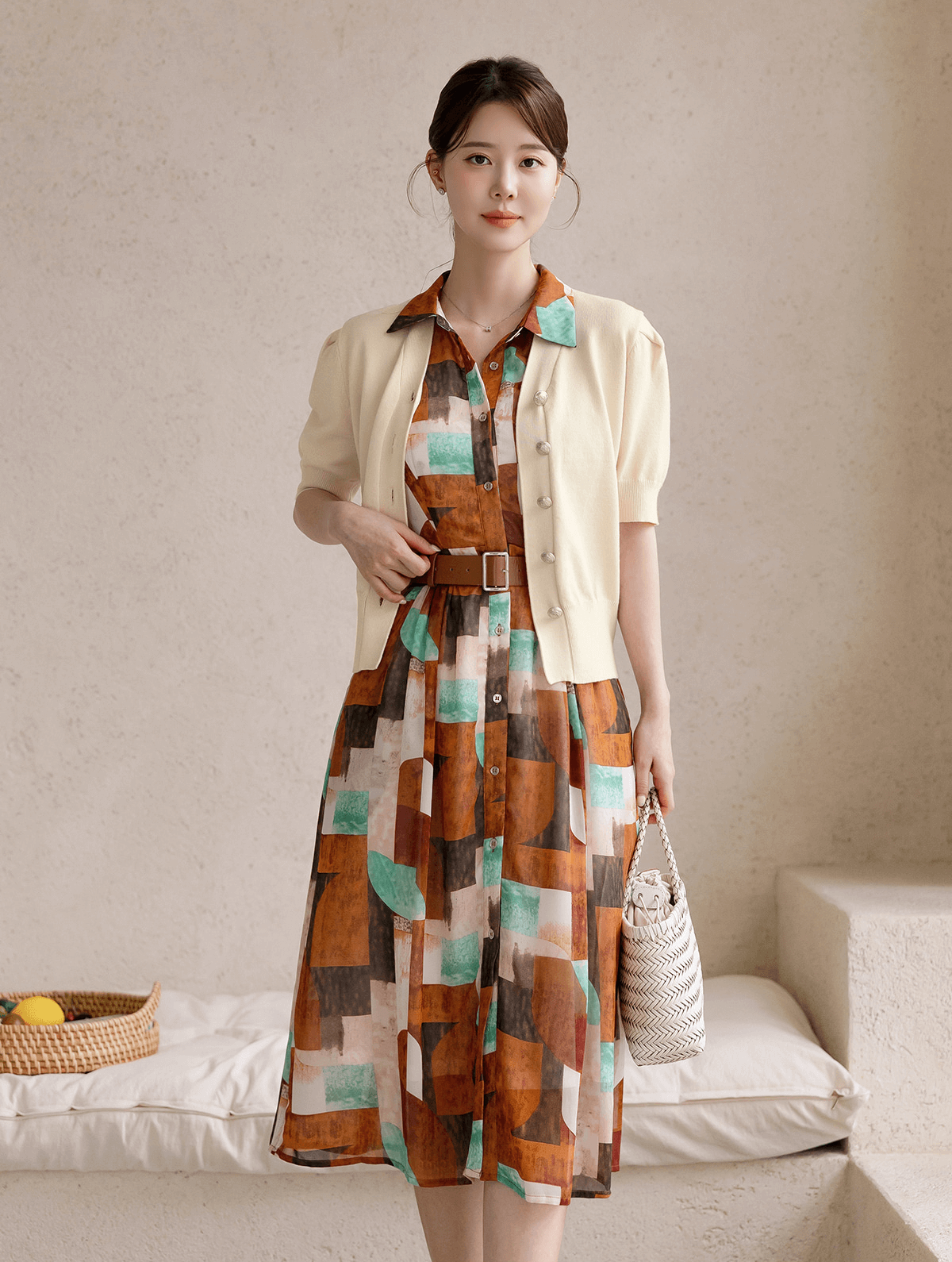 Woman wearing a patterned shirt dress with cap sleeves, classic collar, and faux leather belt, standing in a minimalist setting.