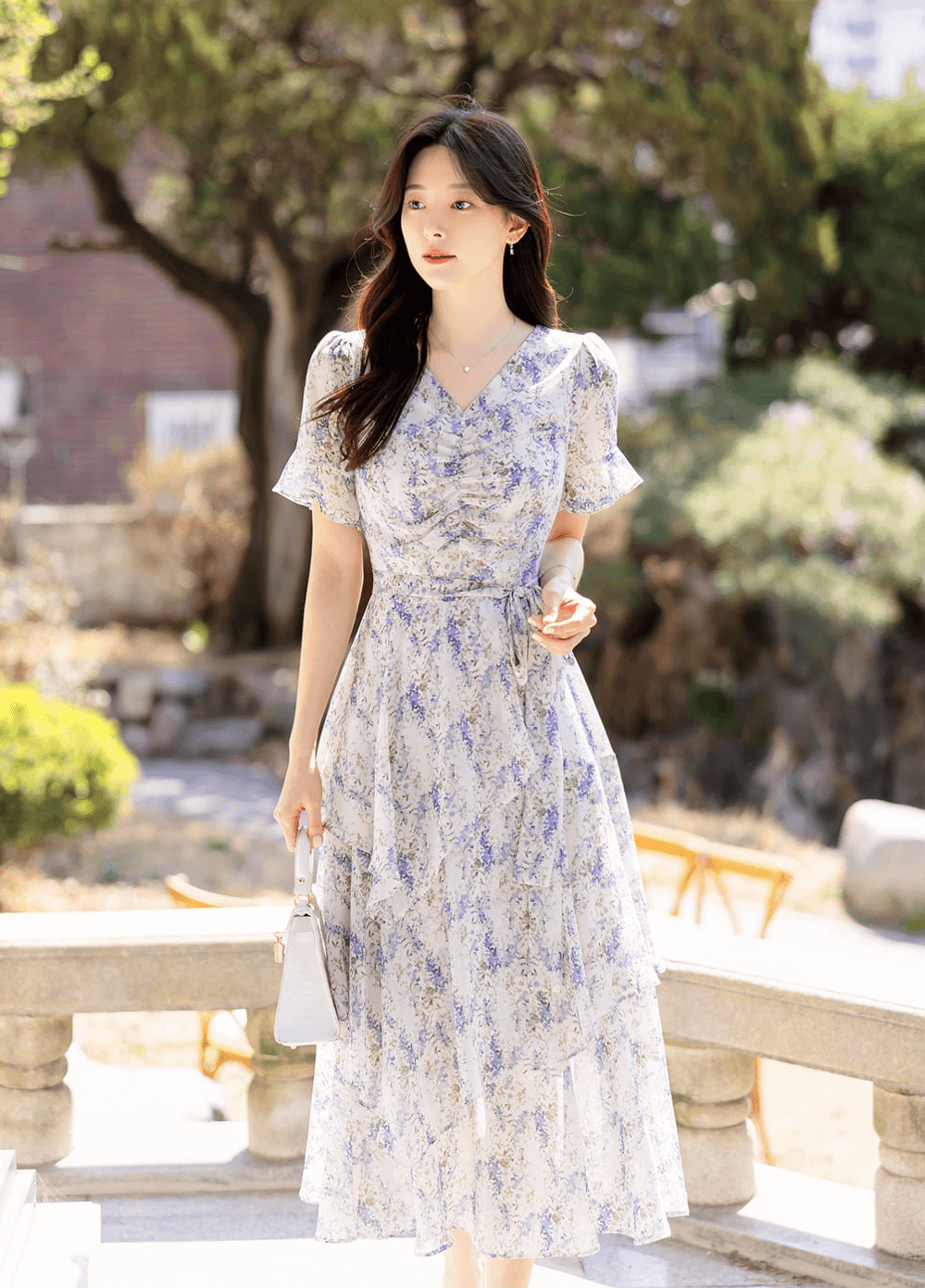 Woman wearing an asymmetrical tiered floral chiffon dress with purple blossoms, featuring a V-neckline and puffed sleeves.