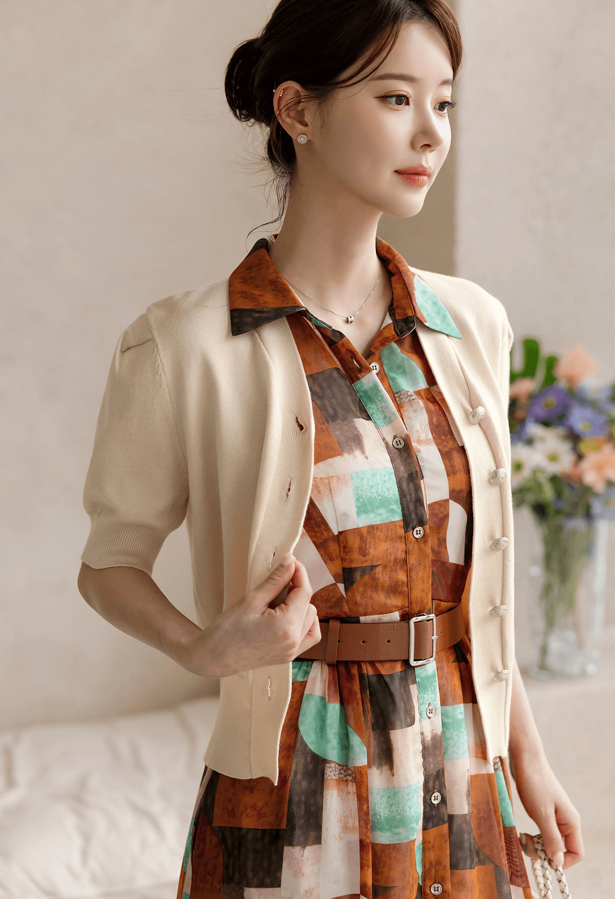 Woman in patterned shirt dress with soft cap sleeves, classic collar, and faux leather belt, styled with cream cardigan.