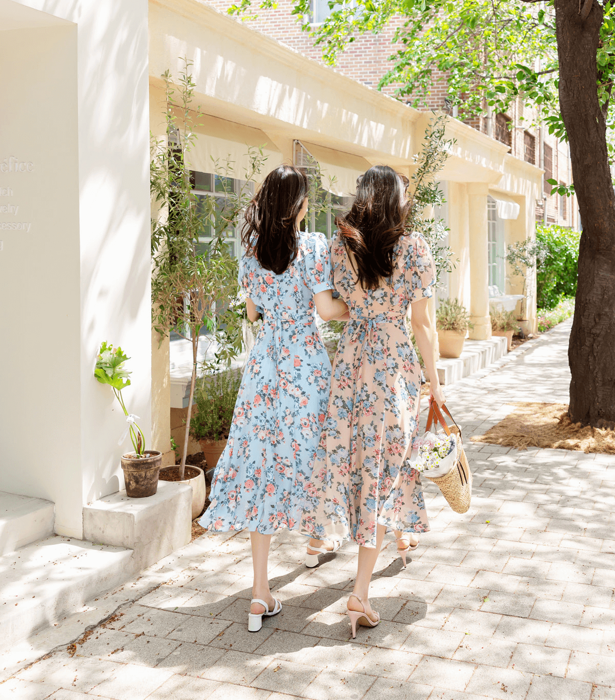 Two women walking in floral chiffon dresses with short puff sleeves and V-necklines, enjoying a sunny day in a charming outdoor setting.