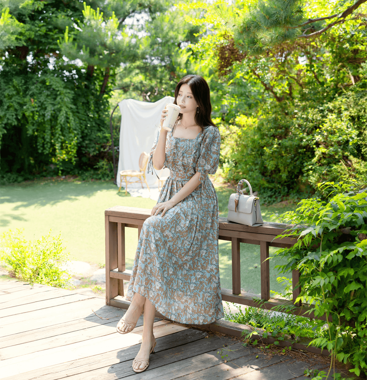 Woman wearing a pleated dress with slit sleeves and ribbon ties, sitting in a garden setting, showcasing the elegant design.