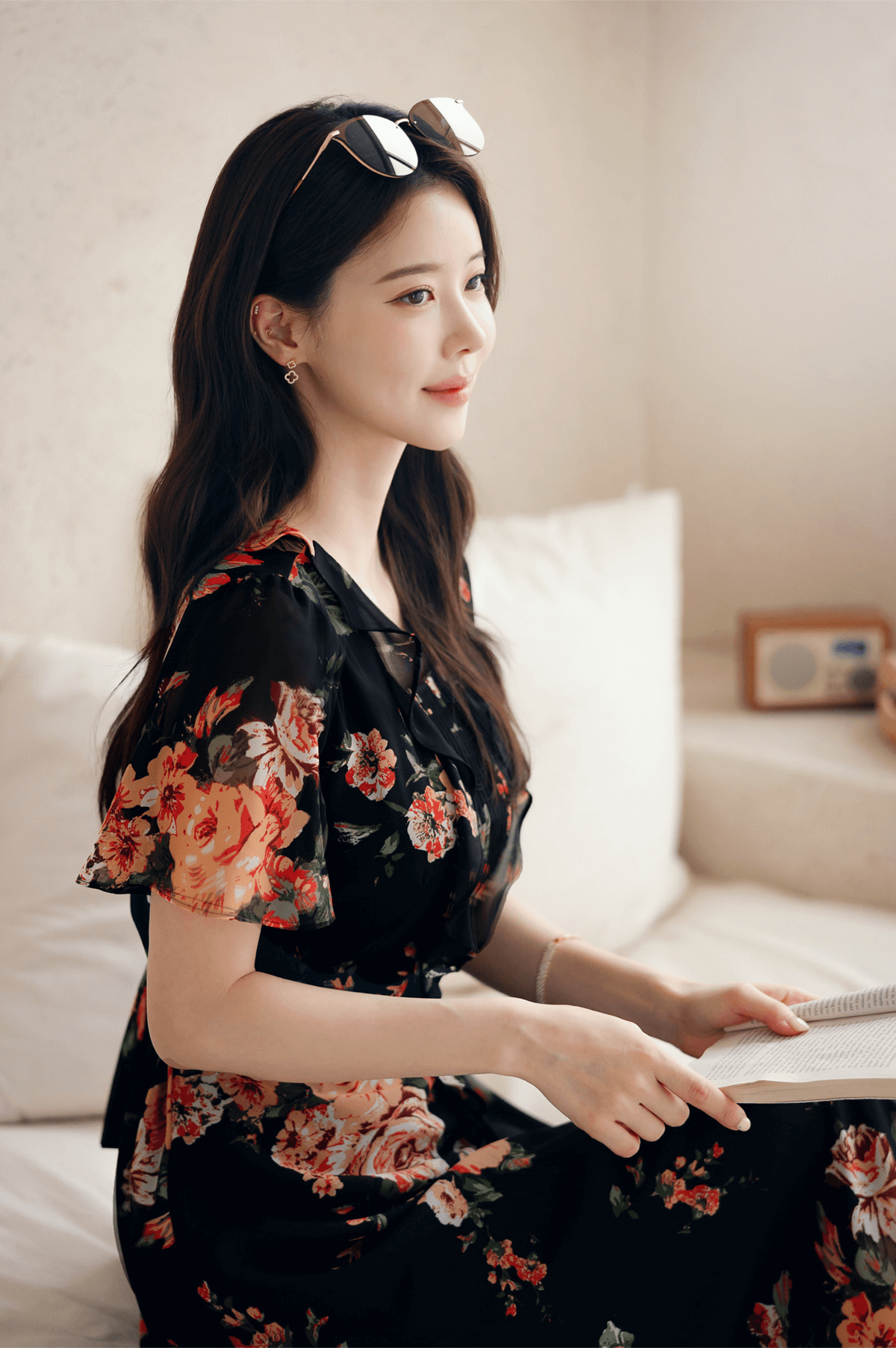 Woman wearing a floral chiffon dress with sheer wing sleeves and a square neckline, sitting and reading in a bright room.