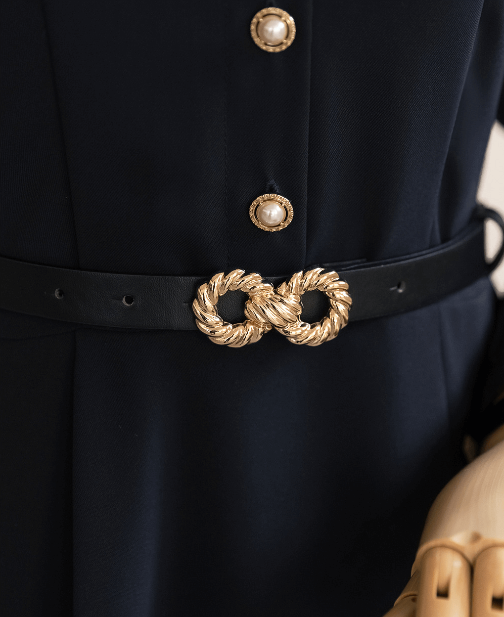 Close-up of elegant navy dress with ornate gold belt buckle and pearl buttons, highlighting refined style and detailed craftsmanship.