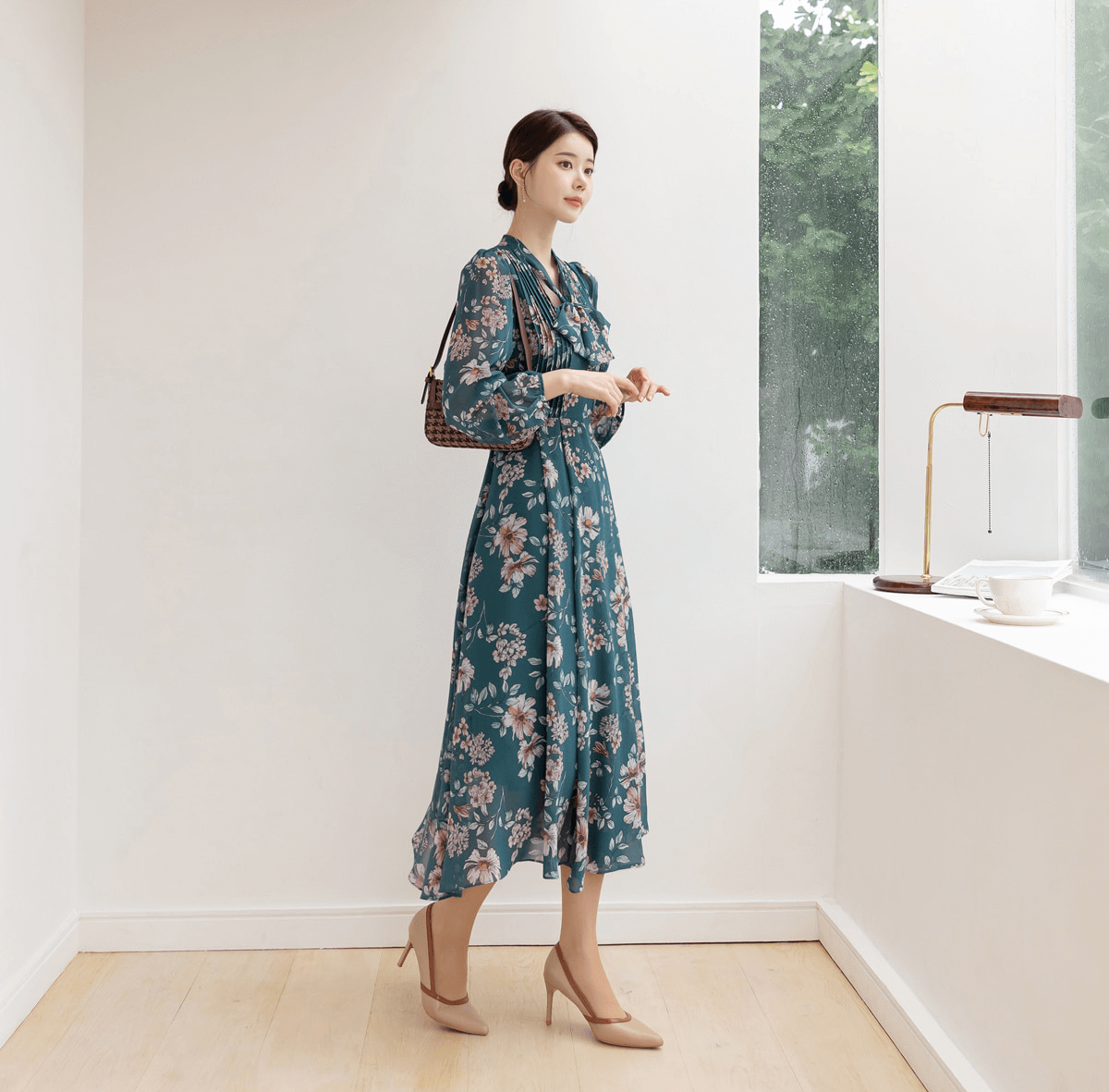 Woman wearing a floral chiffon flare dress with V-neck and convertible neck tie standing by a window.