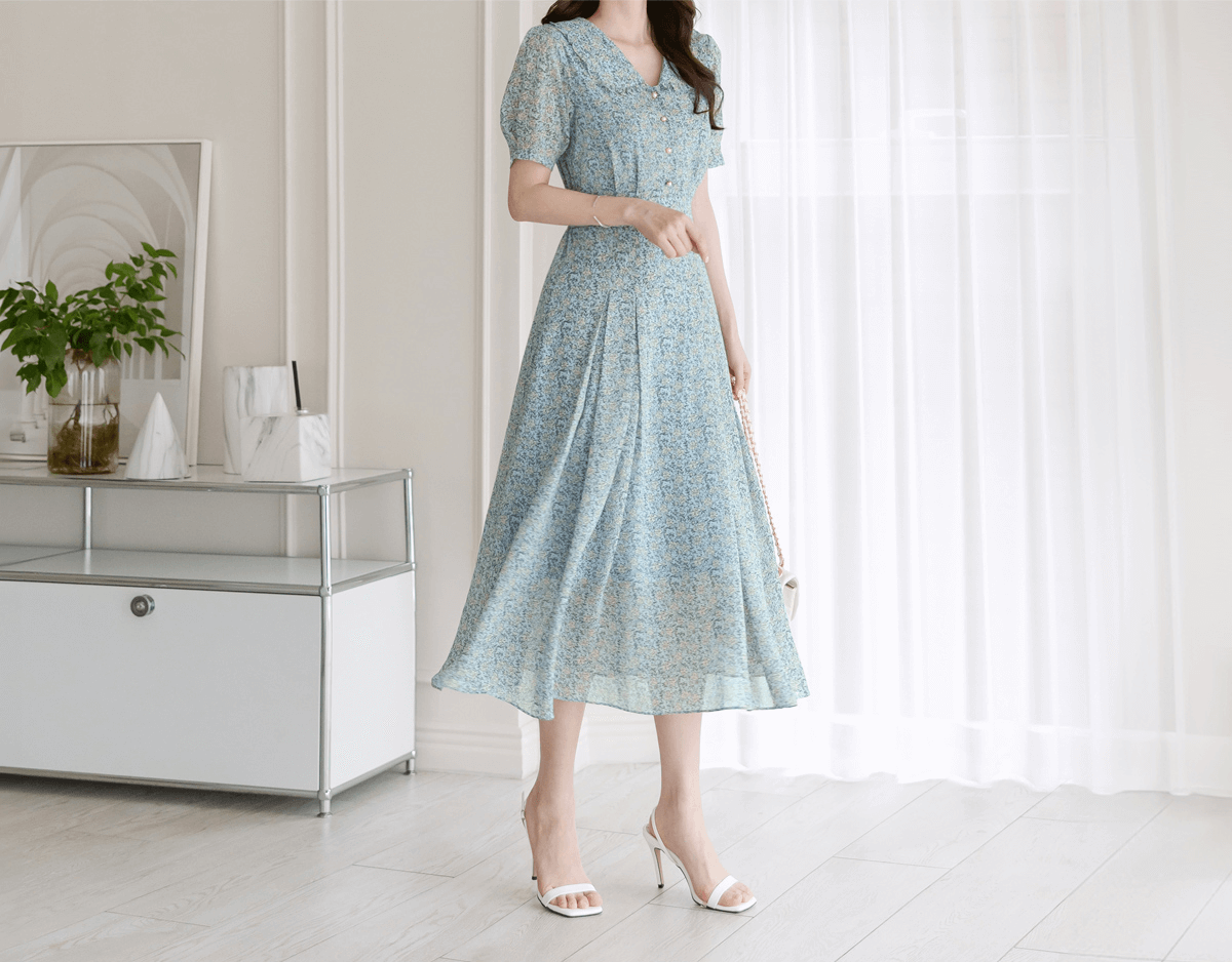 Woman wearing romantic floral chiffon dress with frill collar and waist ribbon in a bright room, showcasing elegant style.