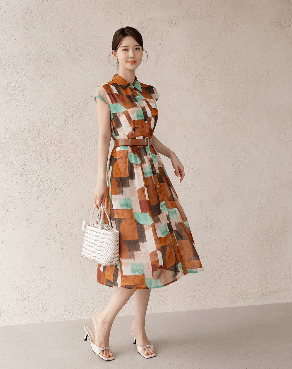 Woman in patterned shirt dress with cap sleeves and belt, holding a white handbag.