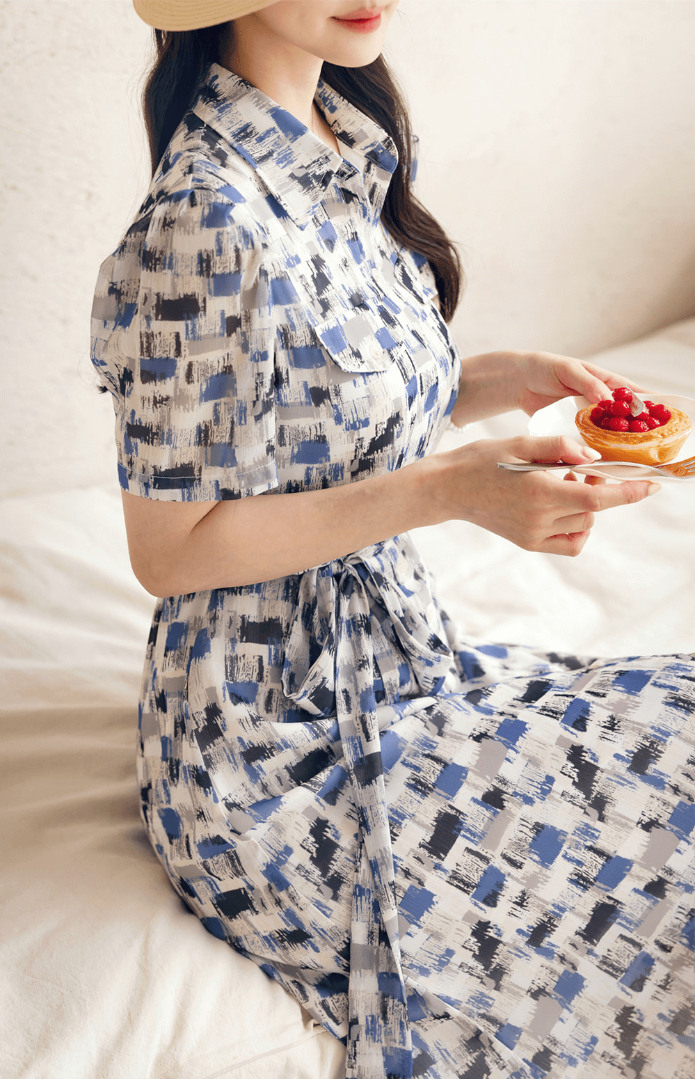 Woman in a blue abstract-patterned chiffon shirt dress with belt, enjoying dessert on a sunny day.