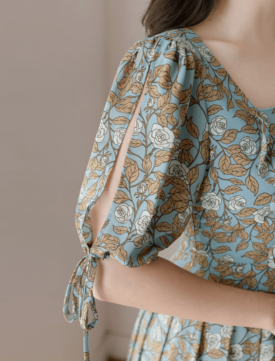 Pleated dress with floral print, featuring shoulder-to-hem slit sleeves and ribbon ties, highlighting elegant design and detail.