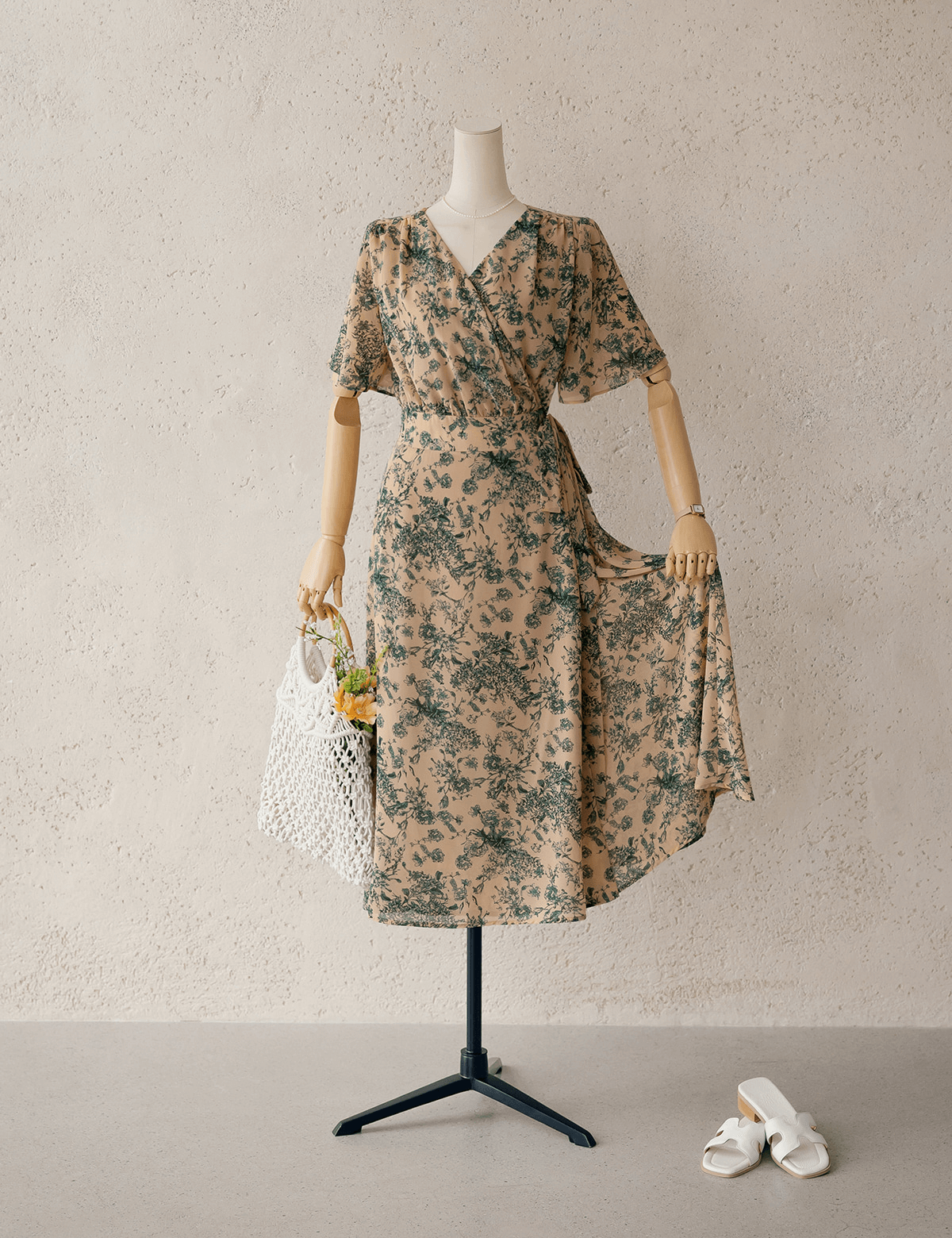 Goddess-inspired wrap dress with wing sleeves on mannequin, featuring a floral design and complimented by a stylish white handbag.