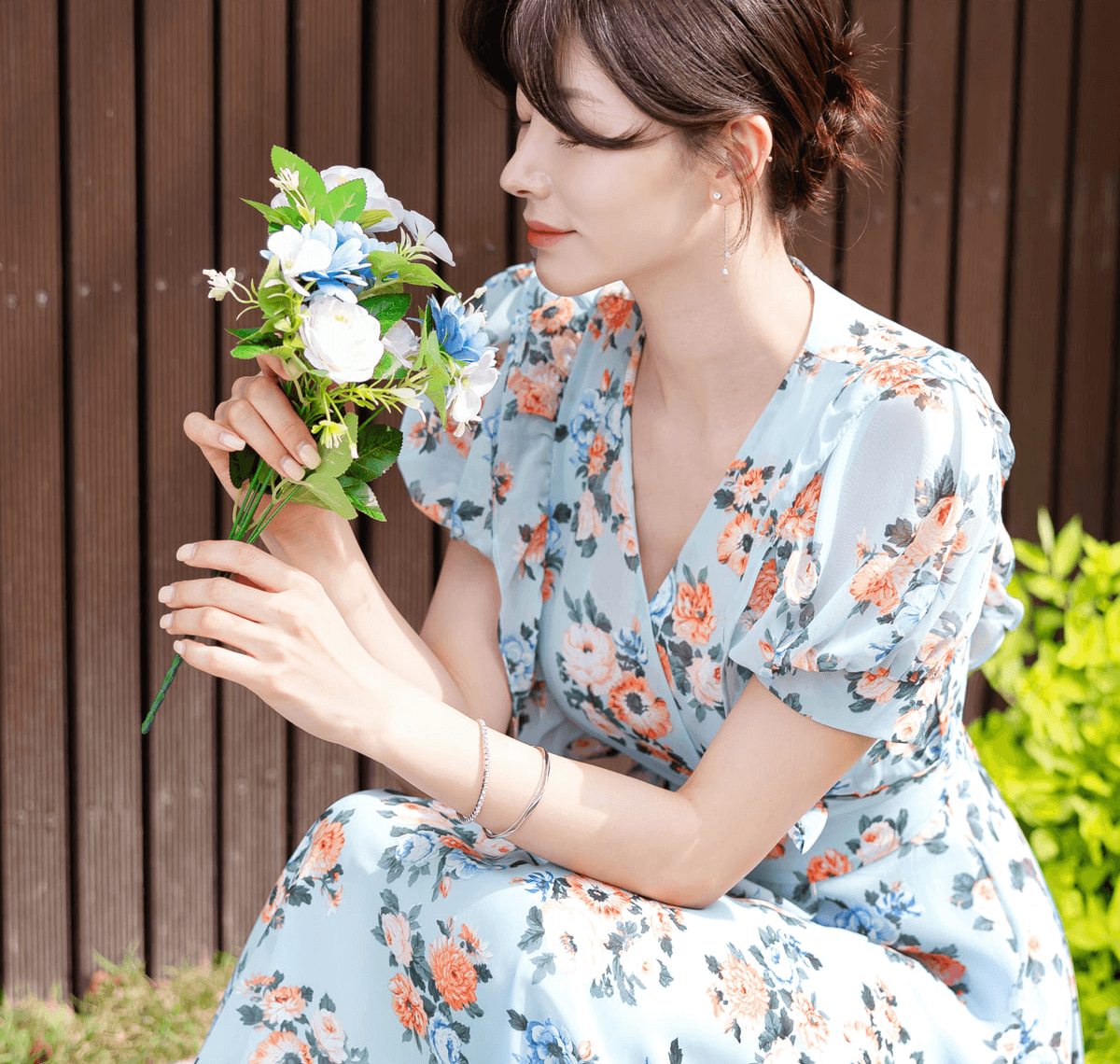 Woman wearing a blue floral chiffon dress with puff sleeves and V-neckline, holding flowers, perfect for spring fashion.