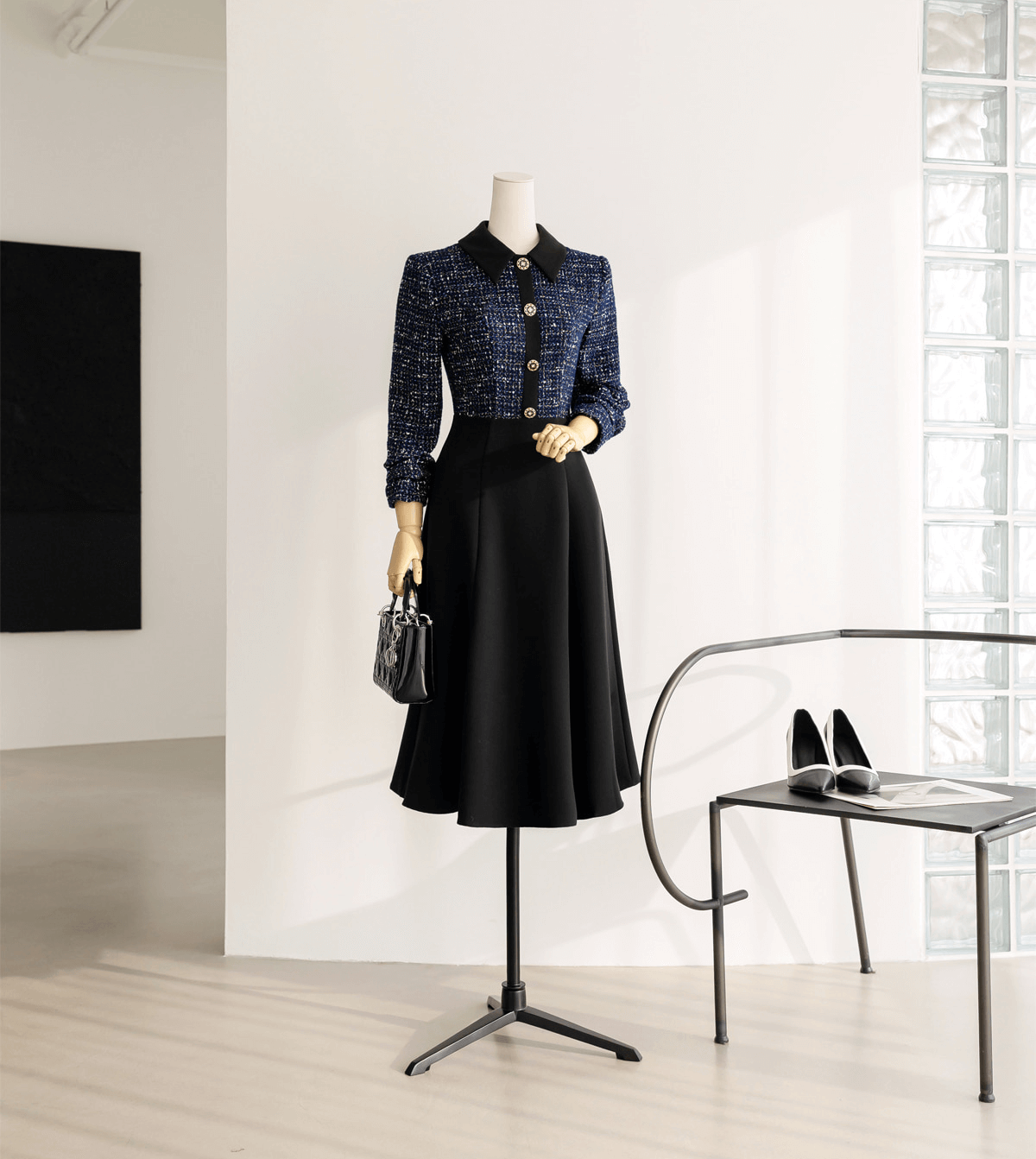 Two-tone tweed and black flare dress with gold button detail displayed on mannequin in modern room; includes handbag and shoes.