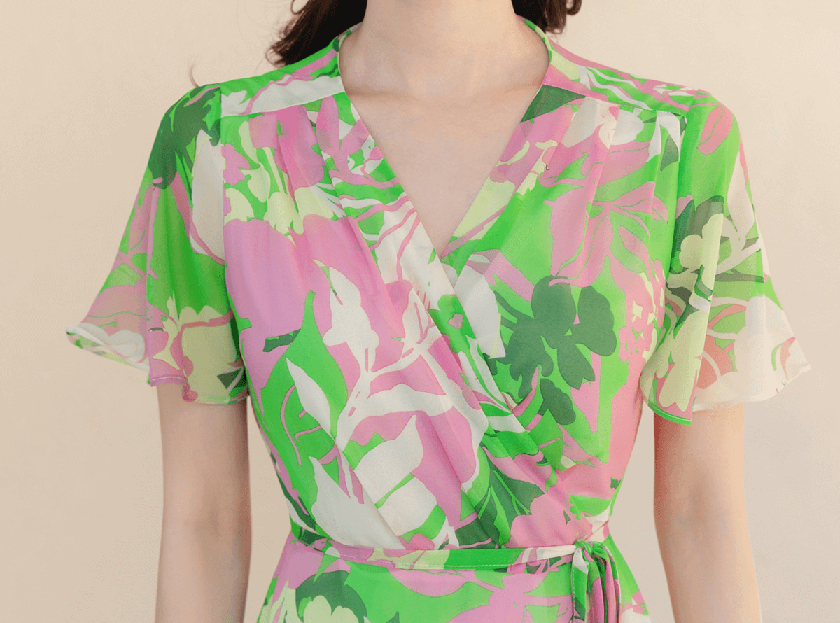 Green chiffon wrap dress with pink and yellow floral print, featuring tulip hem and feminine silhouette for breezy days.