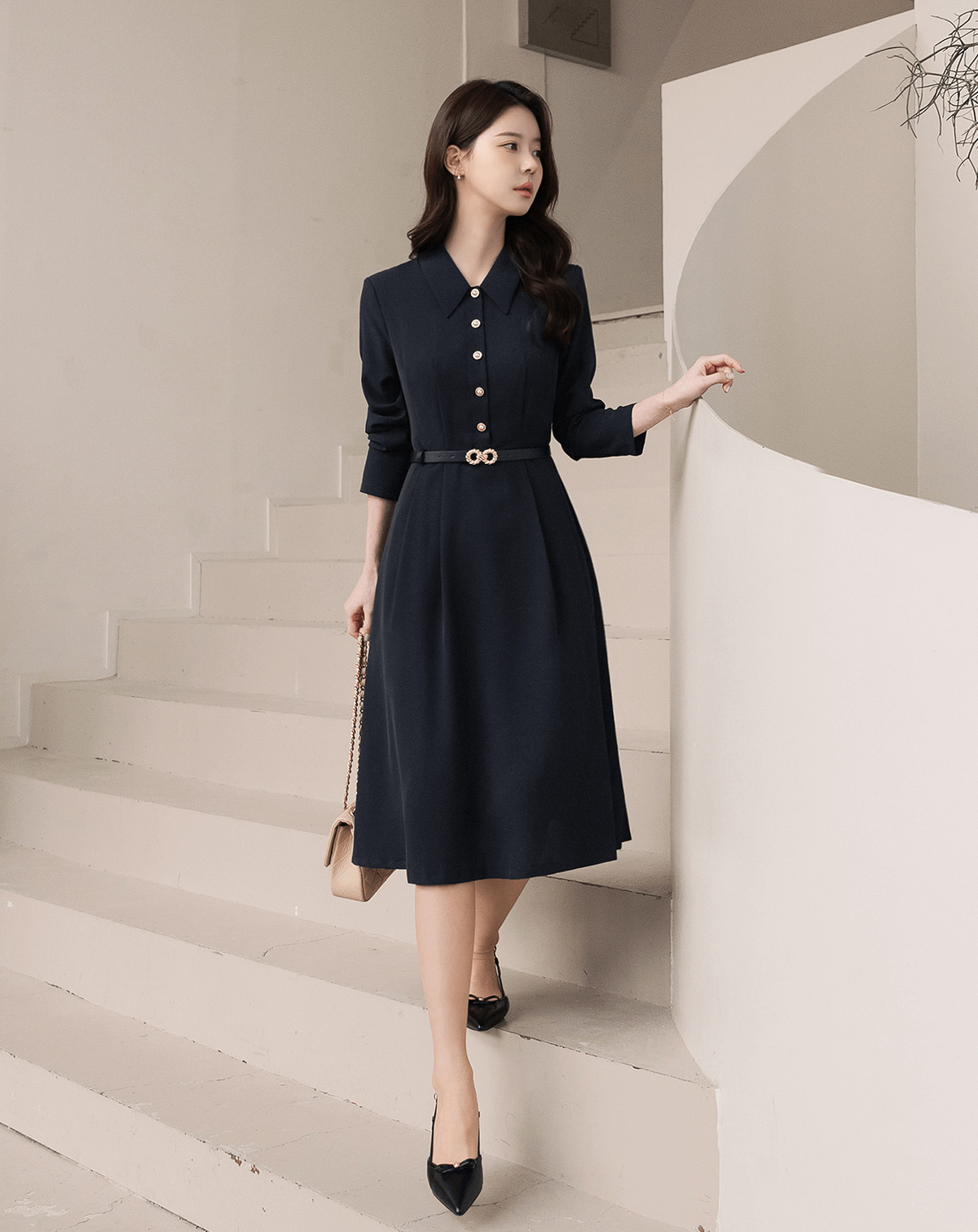 Elegant woman wearing a navy flare dress with long sleeves and belted waist, standing on stairs.