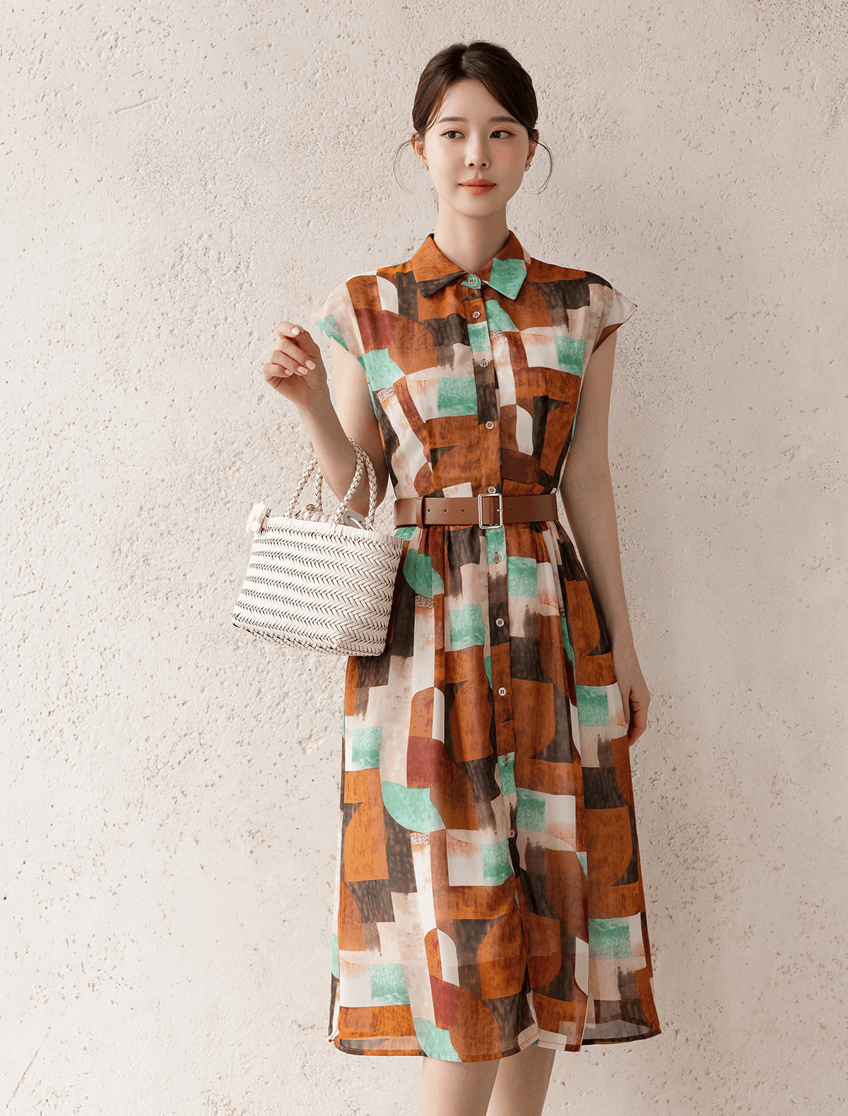 Patterned shirt dress with cap sleeves, classic collar, and a faux leather belt, worn by a model holding a white woven bag.