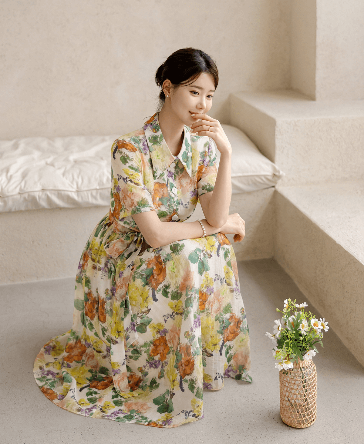 Woman wearing a romantic floral dress with pintuck details and collar neckline, sitting by a vase of flowers, exuding elegance.