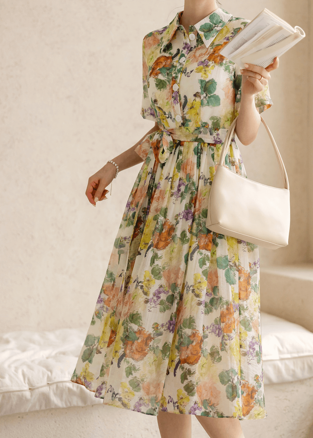 Woman wearing romantic floral dress with pintuck detailing and collar neckline, holding a book and handbag.