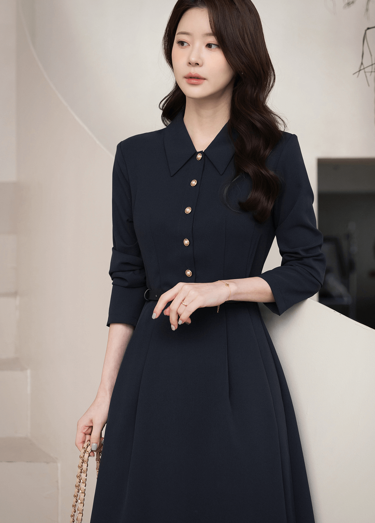 Woman in elegant navy flare dress with long sleeves and belted waist, featuring a tailored collar, perfect for polished occasions.