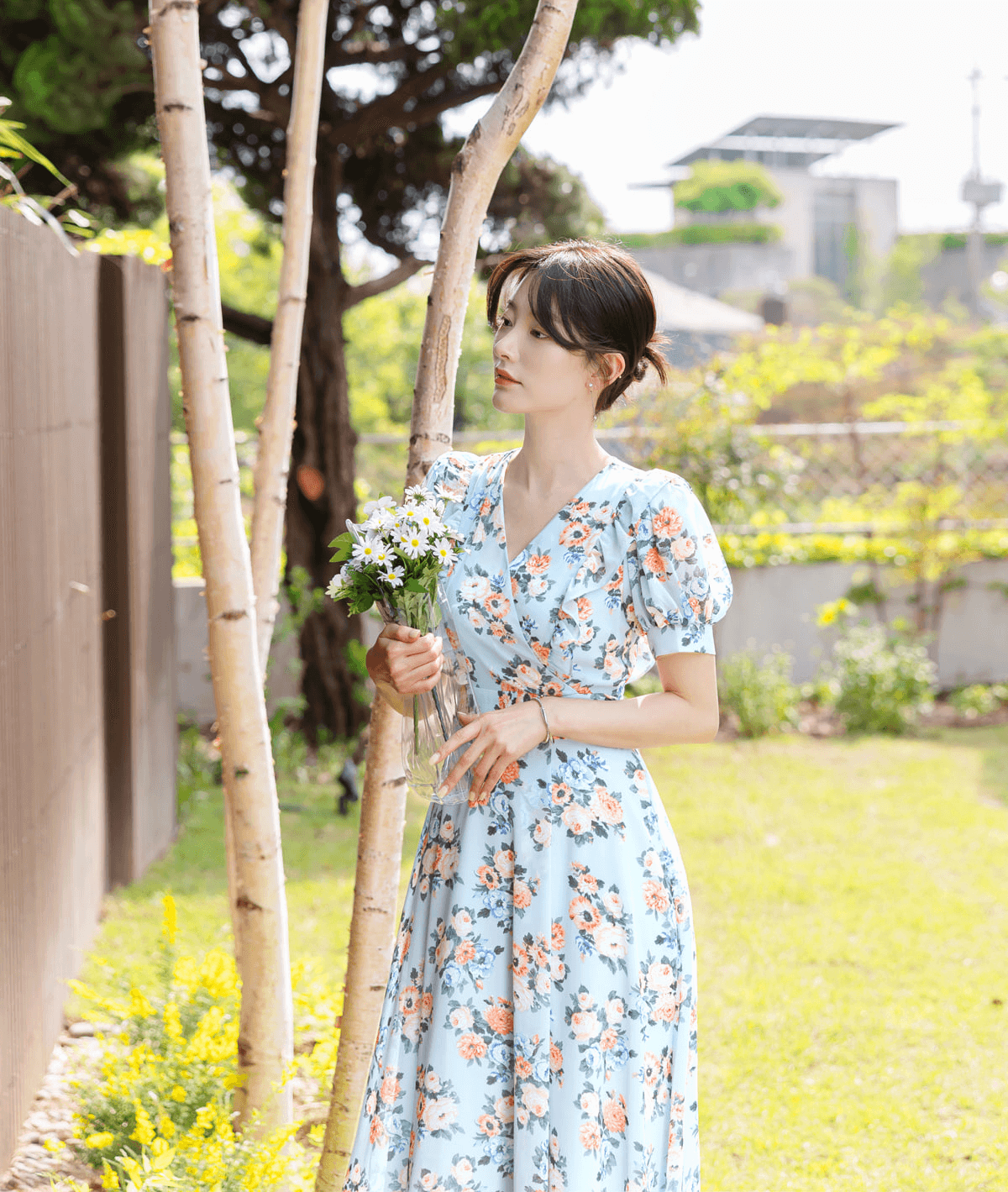 Woman in blue floral chiffon dress with short puff sleeves holding flowers in garden