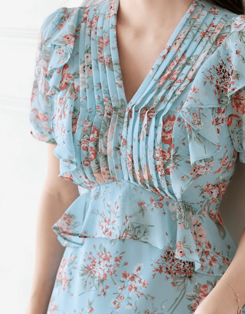 Light sky blue floral chiffon dress with pintuck bodice and peplum detail, featuring softly puffed sleeves and a V-neckline.