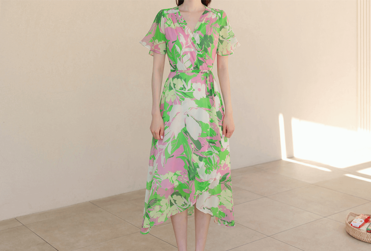 Green chiffon wrap dress with floral patterns, tulip hem, and feminine silhouette, ideal for breezy days and vacations.