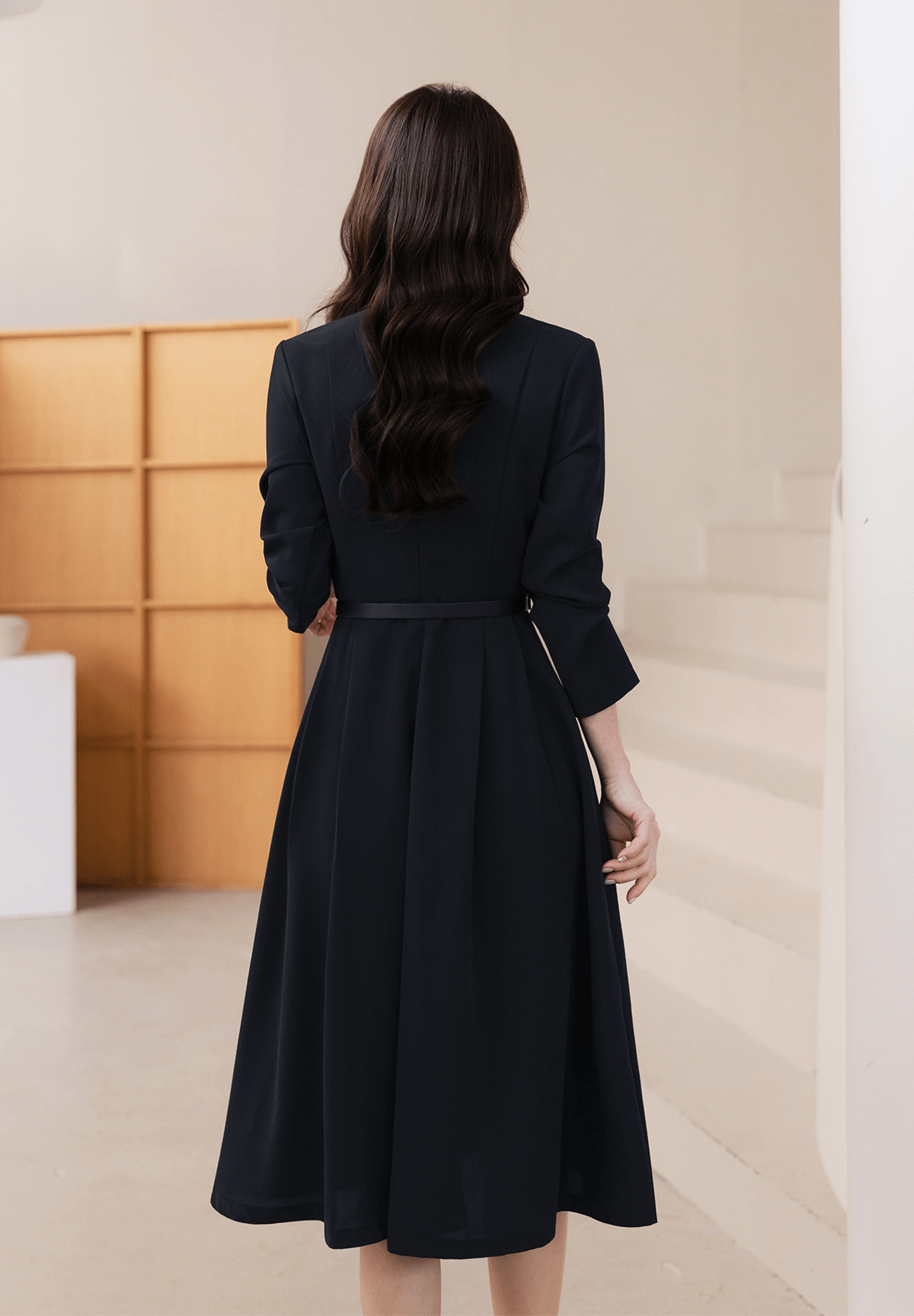 Woman wearing elegant navy flare dress with long sleeves and a belted waist, viewed from the back, showcasing a refined silhouette.