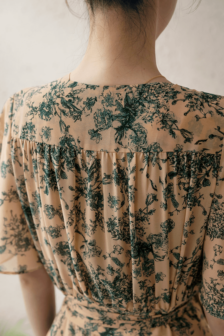 Back view of floral goddess-inspired wrap dress with wing sleeves, featuring elegant green patterns on a beige background.