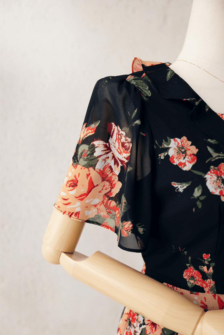 Close-up of floral chiffon dress with sheer wing sleeve and square neckline, black base with pink and orange flowers.