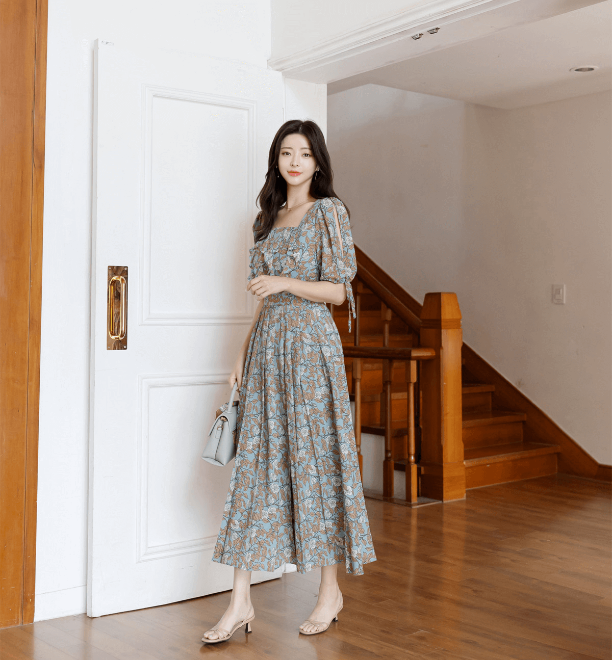 Elegant pleated dress with square neckline and slit sleeves, featuring ribbon ties and an A-line shape, in a stylish indoor setting.