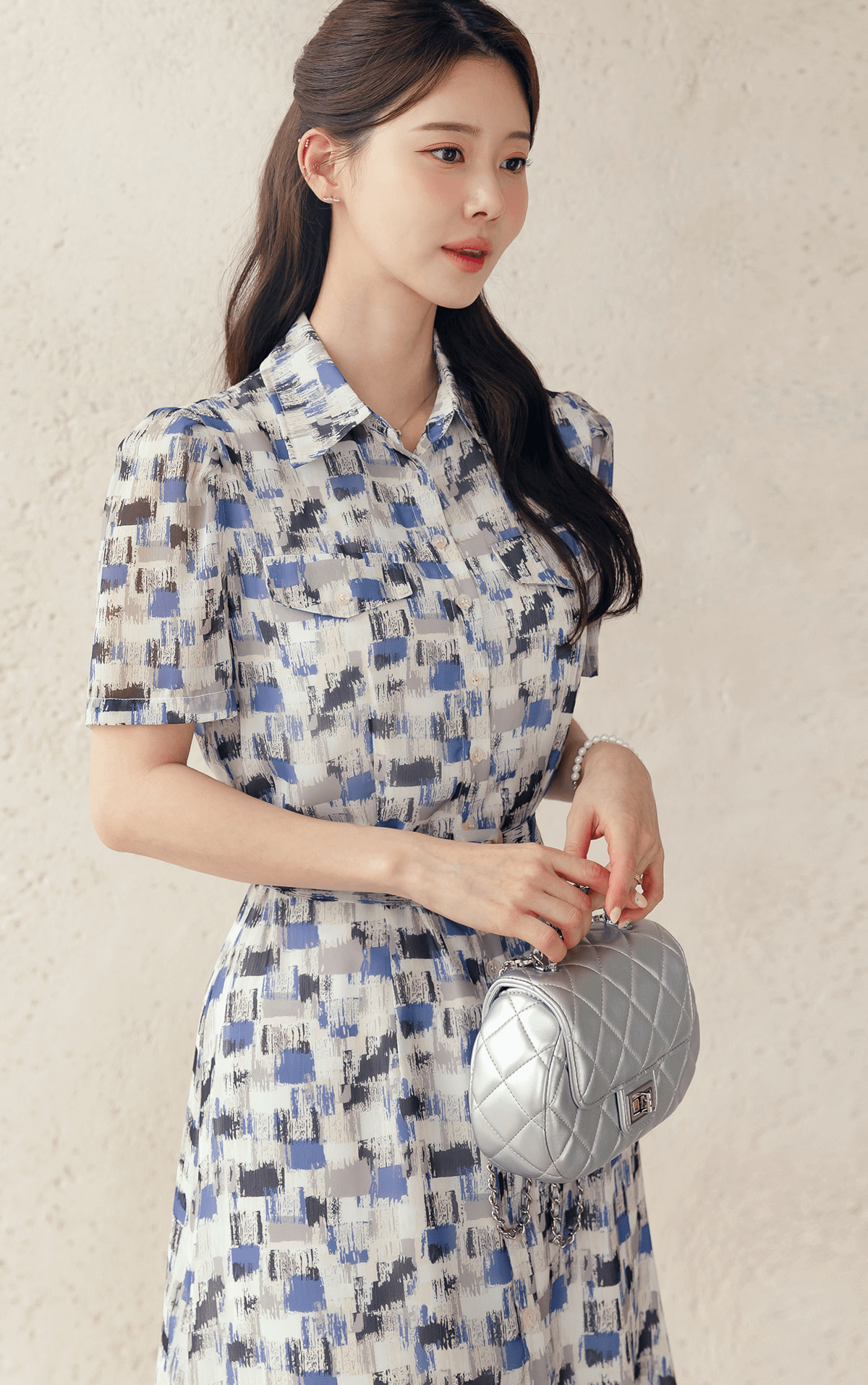 Woman wearing Breezy Chiffon Shirt Dress with blue abstract pattern and matching belt, accessorized with a white quilted handbag.