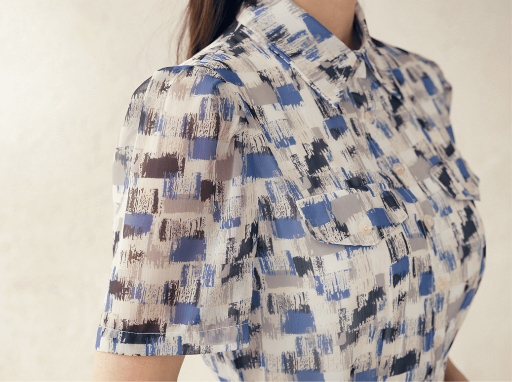 Close-up of a breezy chiffon shirt dress with an abstract blue pattern and collar neckline, highlighting short sleeves and chest pockets.