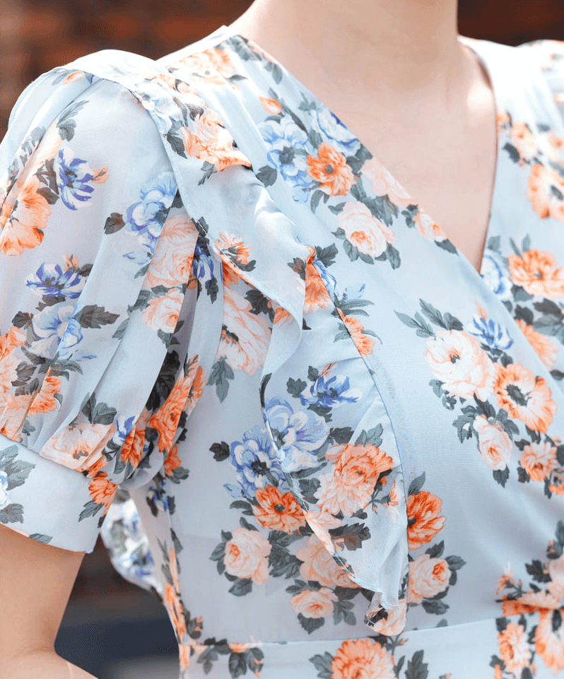 Close-up of romantic floral chiffon dress in blue with short puff sleeves, V-neckline, and orange and blue floral pattern.