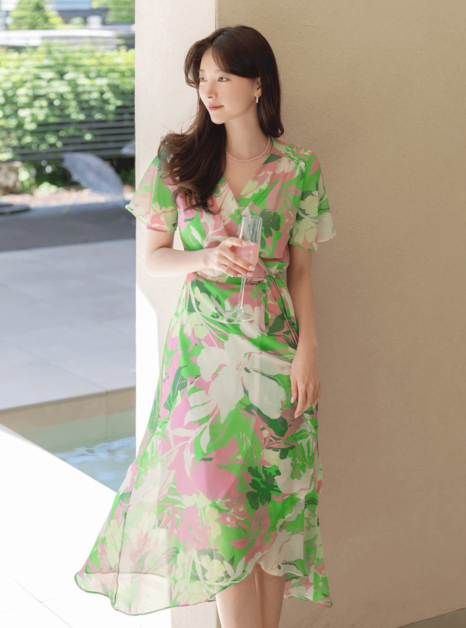 Woman in a green chiffon wrap dress with a tulip hem and floral design enjoying a sunny day.