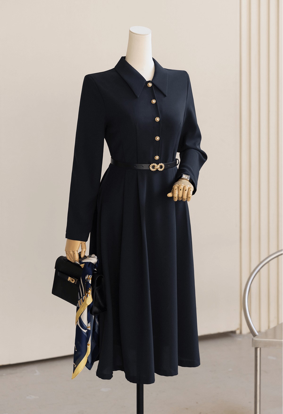 Elegant navy flare dress with long sleeves, belted waist, and structured collar showcased on a mannequin with accessories.