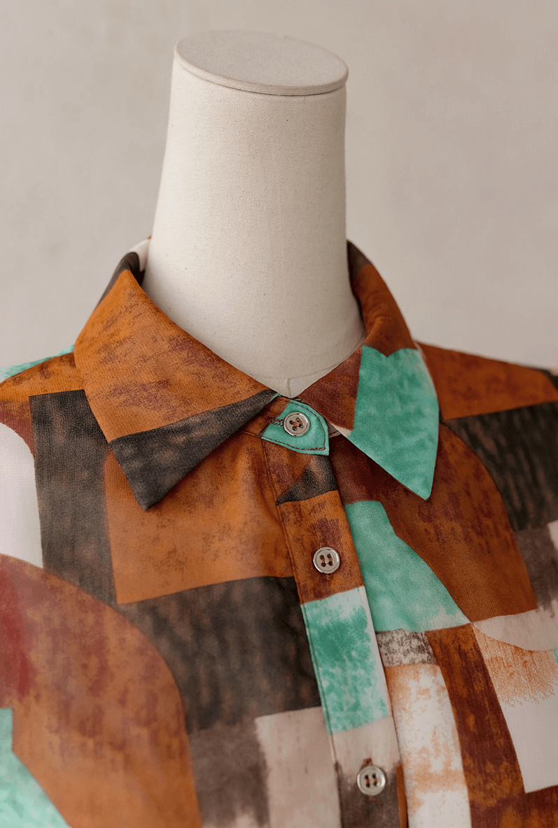 Close-up of shirt dress with classic collar in brown, green, and black geometric pattern on mannequin.
