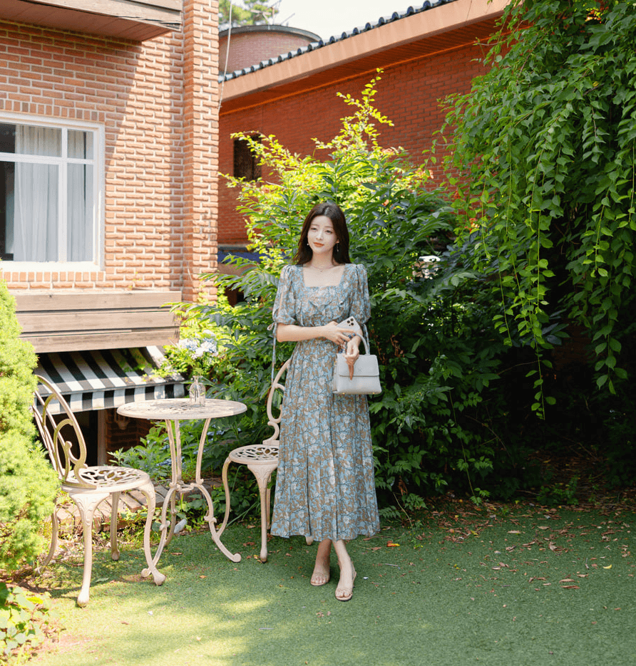 Woman wearing pleated dress with slit sleeves and ribbon ties, standing in a garden setting.