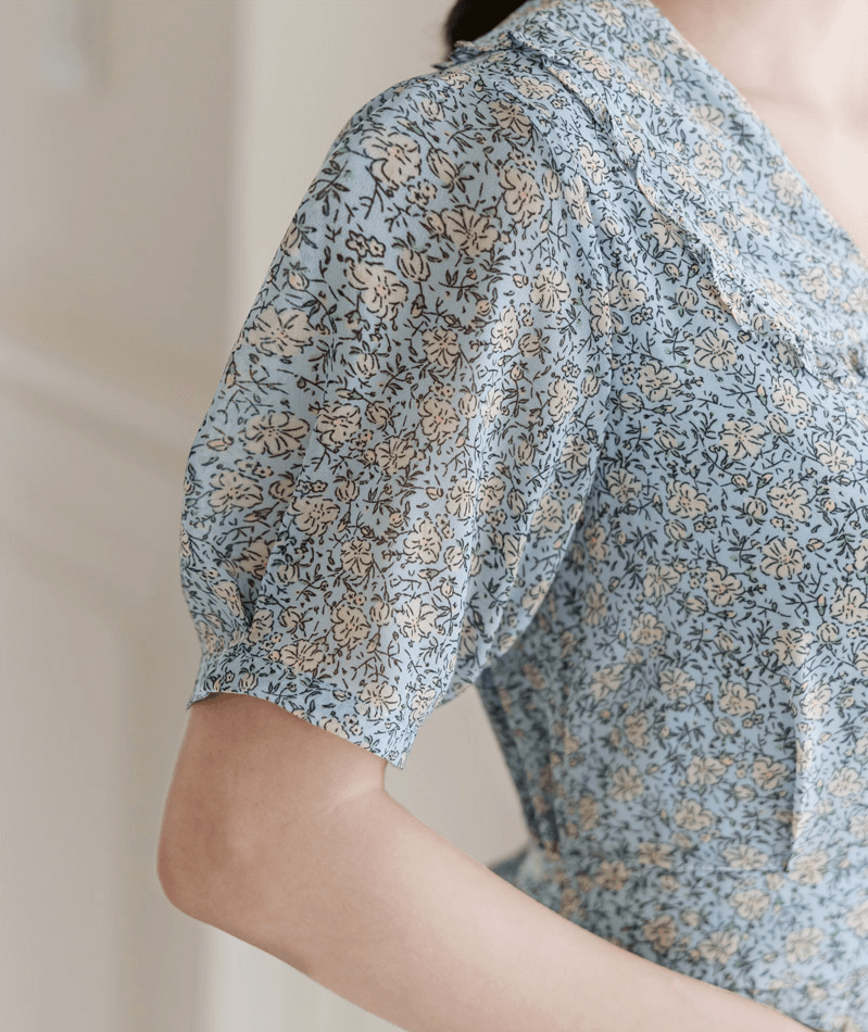 Close-up of a blue floral chiffon dress with a frill collar and short sleeves, featuring elegant waist ribbon ties.