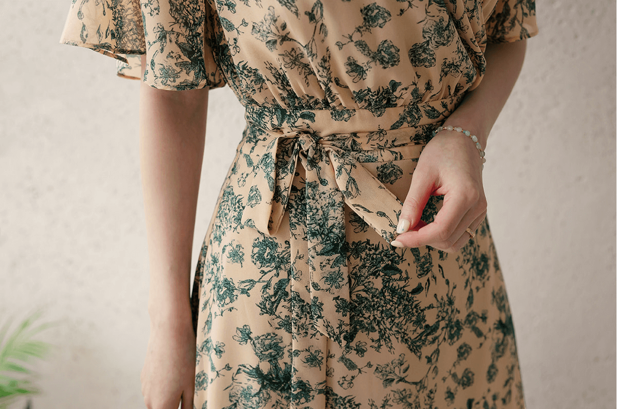Close-up of goddess-inspired wrap dress with floral print and elegant wing sleeves, highlighting adjustable ribbon tie detail.