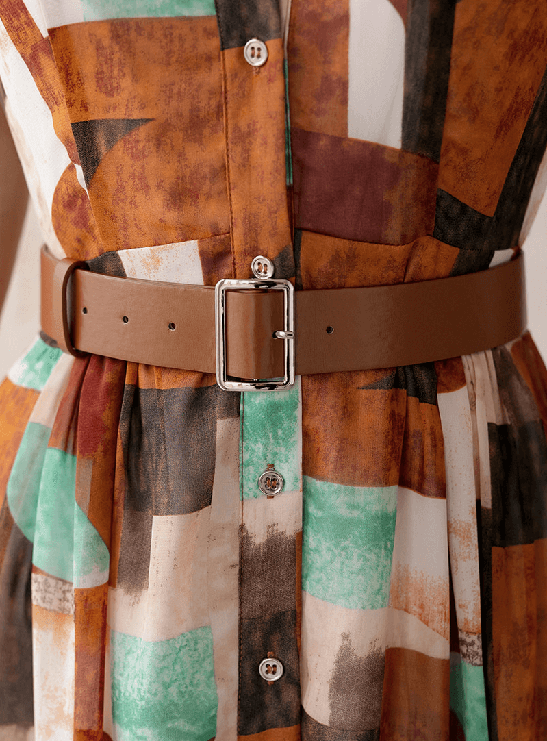 Close-up of a shirt dress with classic collar, soft cap sleeves, and cinched waist by a faux leather belt in artistic print.